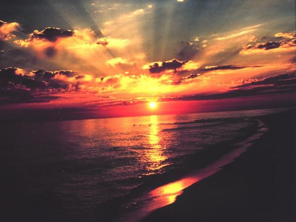 photo of bright sun that is orange above the ocean that reflects the rays of the setting sun.